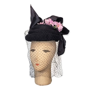 May include: A black felt hat with a large black satin bow and pink flowers. The hat is on a mannequin head with a black veil.