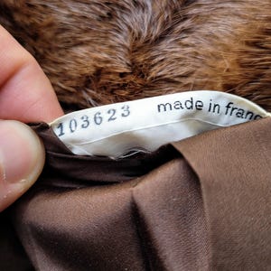 May include: A close-up of a label reading "made in france" and the number "103623". The label is sewn into a brown fabric, with a fur texture visible in the background.