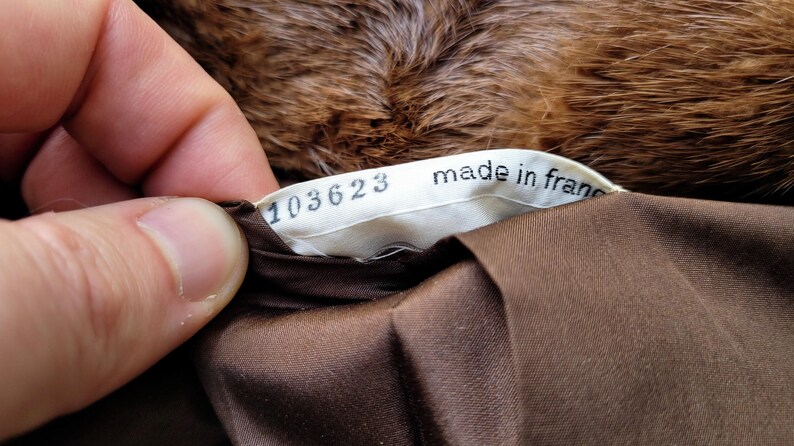 May include: A close-up of a label reading "made in france" and the number "103623". The label is sewn into a brown fabric, with a fur texture visible in the background.