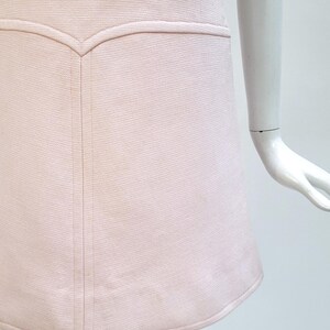 Puede incluir: Vestido rosa p&aacute;lido con tejido texturizado. El vestido presenta un corpi&ntilde;o entallado con un detalle de costura decorativo y una falda acampanada. El dobladillo es ligeramente curvo. El vestido se exhibe en un maniqu&iacute;.