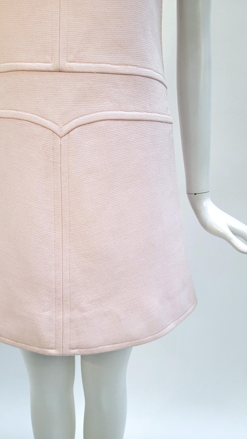 Puede incluir: Vestido rosa p&aacute;lido con tejido texturizado. El vestido presenta un corpi&ntilde;o entallado con un detalle de costura decorativo y una falda acampanada. El dobladillo es ligeramente curvo. El vestido se exhibe en un maniqu&iacute;.