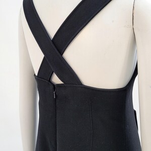 Pu&ograve; includere: Un abito nero con ampie spalline incrociate sulla schiena. L'abito presenta un design semplice ed elegante con un corpetto aderente e una gonna dritta. Le spalline sono spesse e dello stesso materiale.