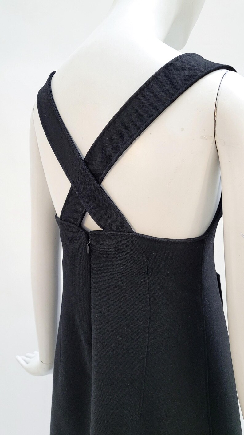 Pu&ograve; includere: Un abito nero con ampie spalline incrociate sulla schiena. L'abito presenta un design semplice ed elegante con un corpetto aderente e una gonna dritta. Le spalline sono spesse e dello stesso materiale.