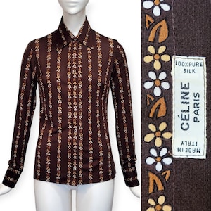 Puede incluir: Una camisa de manga larga a rayas marrones y blancas con cuello abotonado. La camisa tiene un estampado floral y el texto "MADE IN ITALY" y "CELINE PARIS" en el puño. La etiqueta también dice "100% PURE SILK".