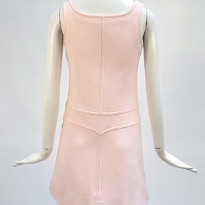 Puede incluir: Vestido rosa claro sin mangas con cuello redondo y corpi&ntilde;o entallado. El vestido presenta una tela texturizada y una falda acampanada. La parte trasera del vestido tiene un detalle de costura vertical. El vestido se exhibe en un maniqu&iacute;.