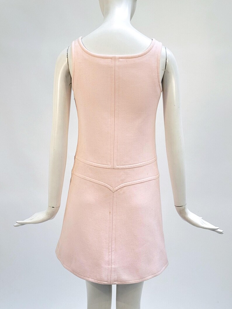 Puede incluir: Vestido rosa claro sin mangas con cuello redondo y corpi&ntilde;o entallado. El vestido presenta una tela texturizada y una falda acampanada. La parte trasera del vestido tiene un detalle de costura vertical. El vestido se exhibe en un maniqu&iacute;.