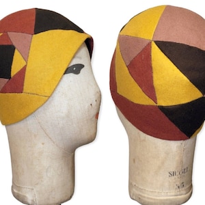 May include: A yellow, brown, red and pink felt hat with a geometric pattern. The hat is on a mannequin head.