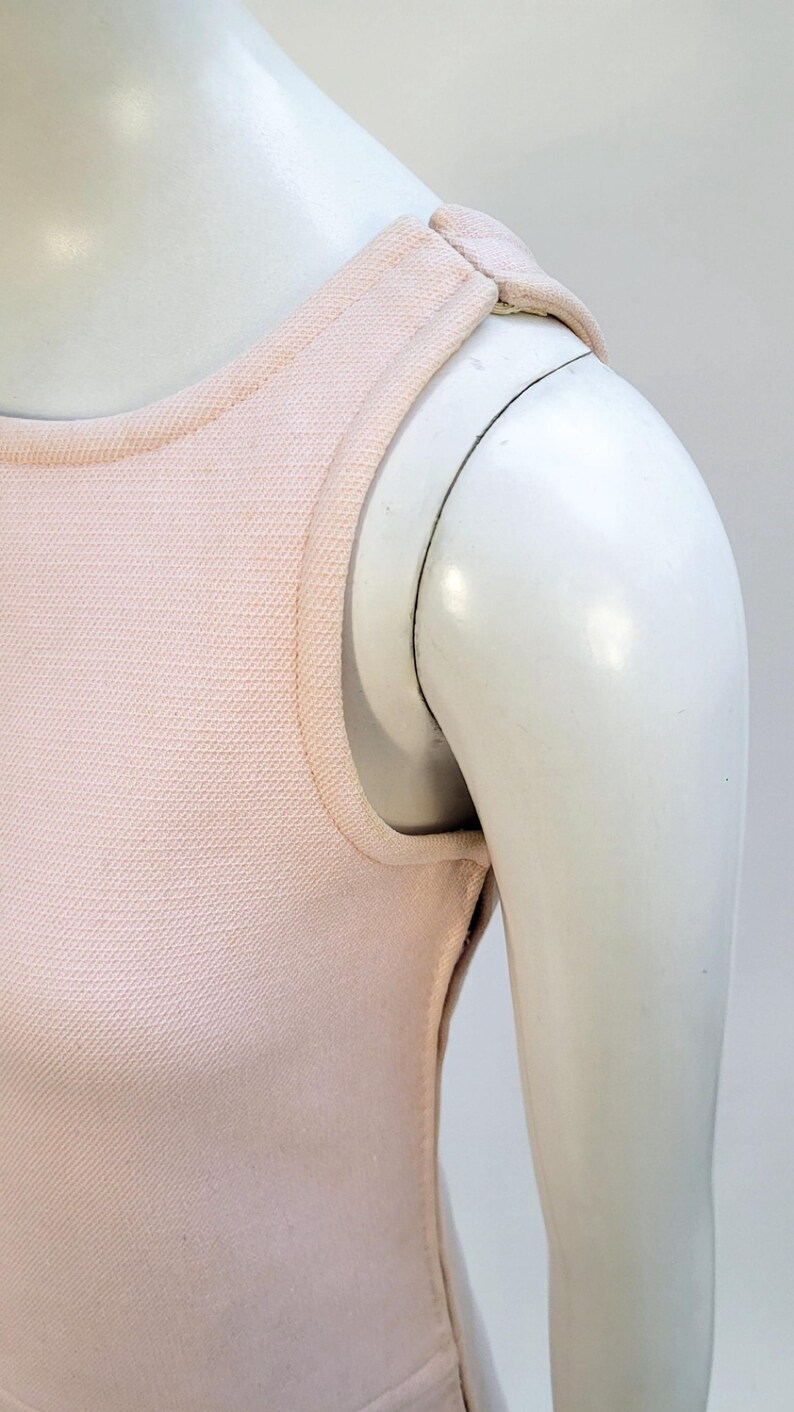 Puede incluir: Un top sin mangas de color rosa claro sobre un maniqu&iacute;. El top tiene una tela texturizada y un escote redondo. Las correas de los hombros son una extensi&oacute;n del escote. Se ve el brazo del maniqu&iacute;.