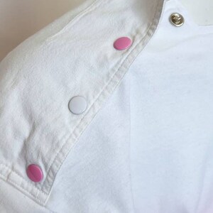 May include: White shirt with a pink and white ombre design. The shirt has a white collar and a row of pink and white buttons down the shoulder seam.