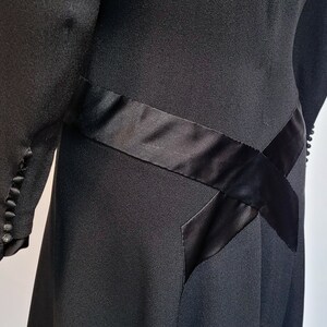 Puede incluir: Vestido negro con un detalle de cinta de sat&eacute;n. La cinta est&aacute; cosida en forma de cruz en la falda.