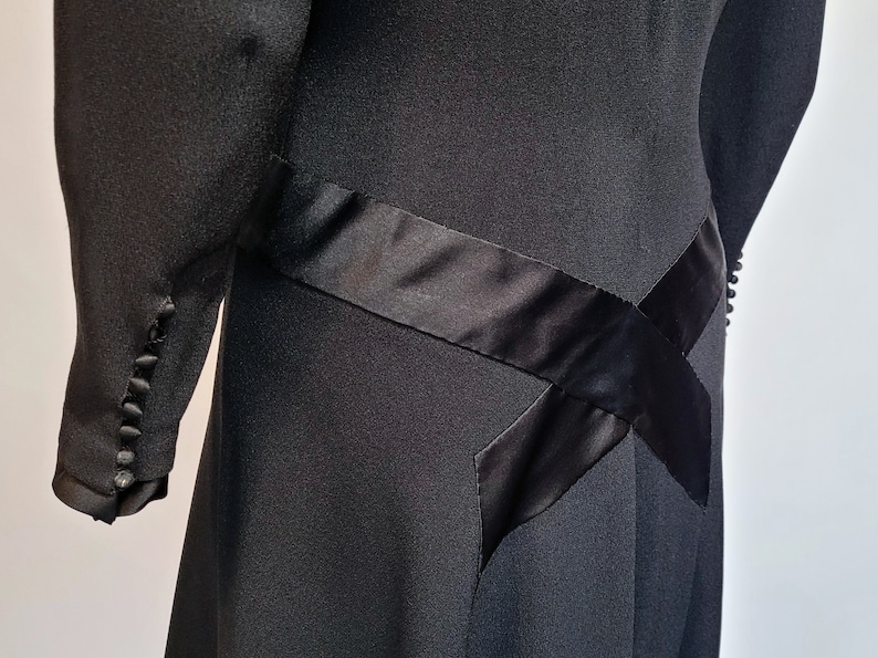 Puede incluir: Vestido negro con un detalle de cinta de sat&eacute;n. La cinta est&aacute; cosida en forma de cruz en la falda.