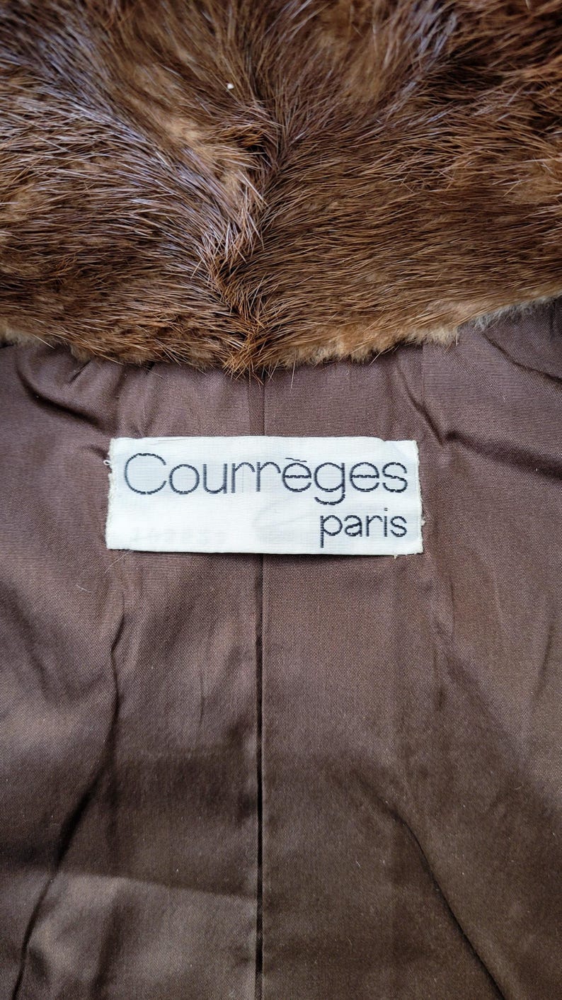 May include: A close-up shot of a brown fur collar and a brown fabric lining. The lining has a label with the text "Courr&egrave;ges paris" in a white rectangle.