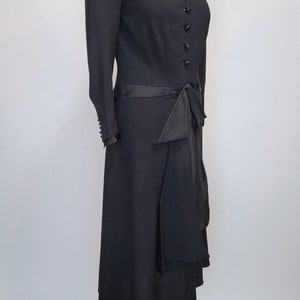 Puede incluir: Un vestido negro con cuello de sat&eacute;n y un lazo de sat&eacute;n en la cintura. El vestido tiene un corpi&ntilde;o ajustado y una falda fluida.