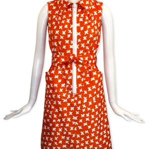 May include: A sleeveless orange dress with a white geometric pattern. The dress has a white collar, a zipper down the front, and a belt that ties at the waist.