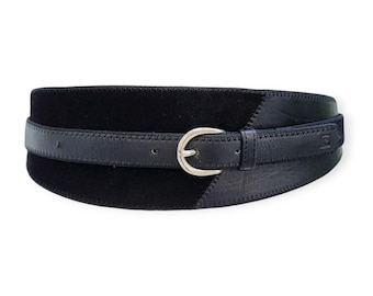 May include: A wide black belt with a silver-colored buckle. The belt features a suede-like center section and a smooth leather strap that fastens with a classic buckle. The design is a combination of textures and materials.