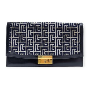 Può includere: Una pochette rettangolare nera con chiusura dorata. La patta superiore presenta un motivo geometrico blu navy e crema. La pochette è realizzata in pelle e ha una chiusura a serratura dorata.