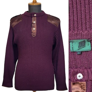 Może przedstawiać: Bordowy sweter z dzianiny o prążkowanym splocie, z brązowymi skórzanymi akcentami i zapięciem na guziki przy szyi. Sweter ma dwa brązowe skórzane naszywki na ramionach. Etykieta zawiera napis "Junior Gaultier" i "Made in Italy".