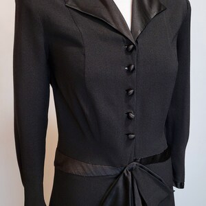 Puede incluir: Un vestido negro con cuello y lazo de sat&eacute;n. El vestido tiene mangas largas y un corpi&ntilde;o ajustado. El vestido se abrocha con botones en la parte delantera.