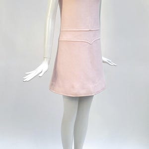 Puede incluir: Vestido rosa p&aacute;lido sin mangas sobre un maniqu&iacute;. El vestido presenta un corpi&ntilde;o ajustado con costuras verticales y una falda ligeramente acampanada. El dise&ntilde;o es simple y elegante, ideal para un look vintage o retro.