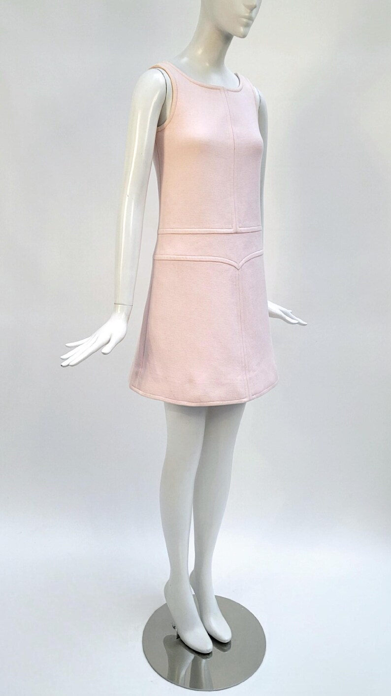 Puede incluir: Vestido rosa p&aacute;lido sin mangas sobre un maniqu&iacute;. El vestido presenta un corpi&ntilde;o ajustado con costuras verticales y una falda ligeramente acampanada. El dise&ntilde;o es simple y elegante, ideal para un look vintage o retro.