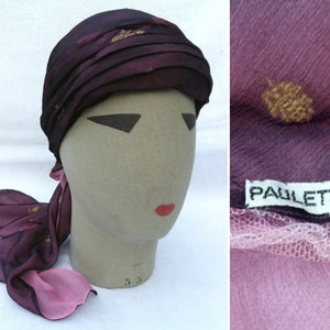 May include: A purple and pink silk turban with gold leaf accents. The turban is tied with a long scarf and has a label that reads "Paulette".