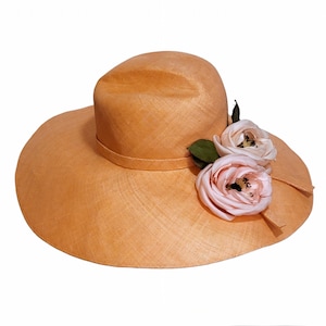 May include: A wide-brimmed straw hat in a light peach colour with two pink fabric roses attached to the side.
