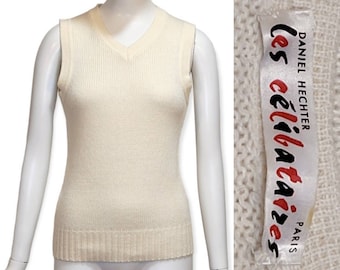 Può includere: Un maglione bianco senza maniche con scollo a V. Il maglione ha una trama a coste e un'etichetta che recita "Daniel Hechter Les Celibataires Paris".