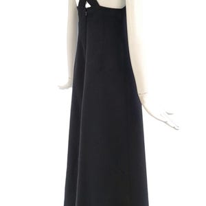 Pu&ograve; includere: Un abito nero con un esclusivo design a bretelle incrociate sulla schiena. L'abito ha una silhouette semplice ed elegante e una gonna fluida. L'abito &egrave; esposto su un manichino su sfondo bianco.