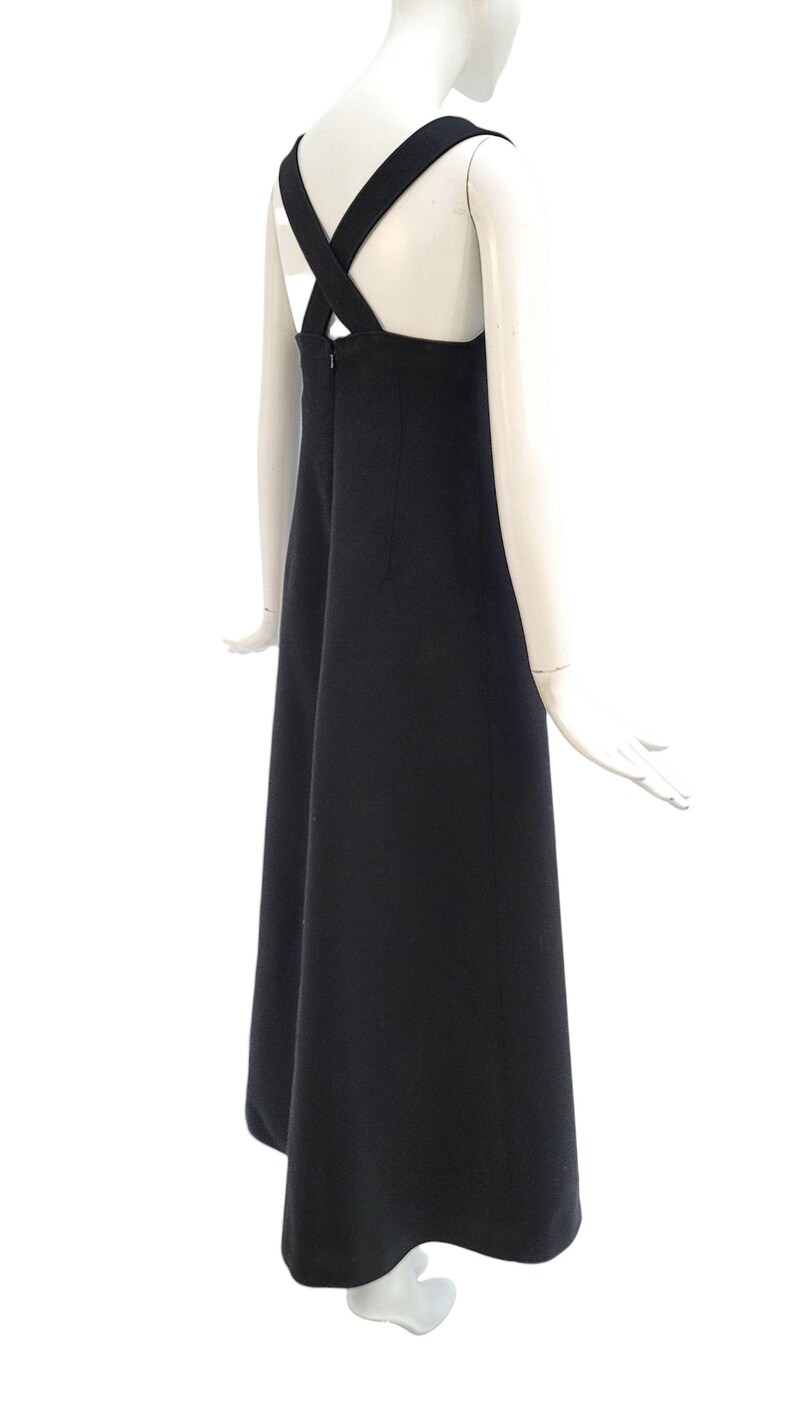 Pu&ograve; includere: Un abito nero con un esclusivo design a bretelle incrociate sulla schiena. L'abito ha una silhouette semplice ed elegante e una gonna fluida. L'abito &egrave; esposto su un manichino su sfondo bianco.