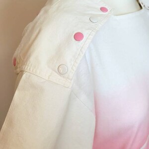 May include: White short-sleeved shirt with pink ombre design and white buttons on the shoulder.