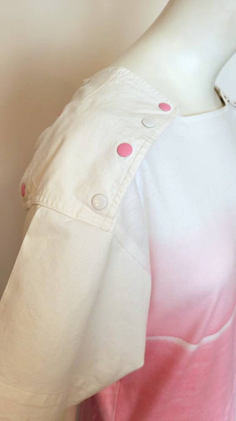 May include: White short-sleeved shirt with pink ombre design and white buttons on the shoulder.