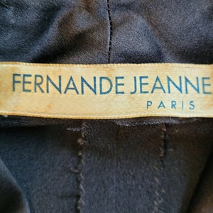 Puede incluir: Primer plano de una etiqueta de tela marr&oacute;n con el texto "Fernande Jeanne Paris" en letras azules.