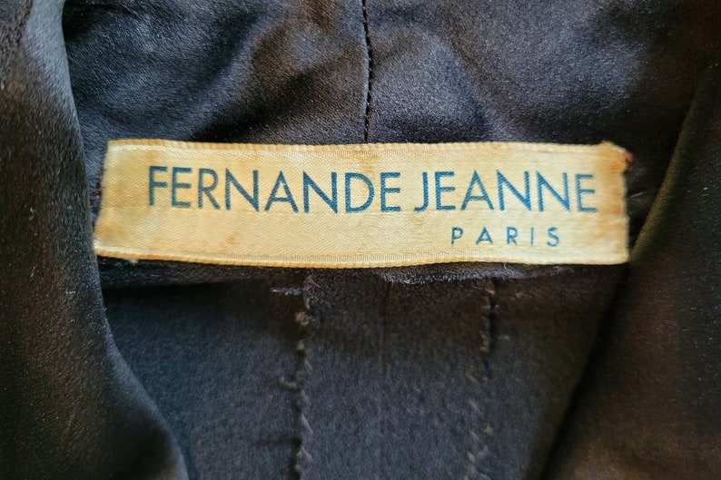 Puede incluir: Primer plano de una etiqueta de tela marr&oacute;n con el texto "Fernande Jeanne Paris" en letras azules.