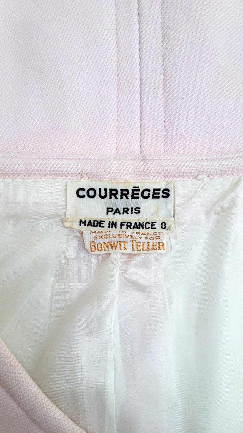 Puede incluir: Primer plano de una tela rosa claro con forro blanco. La etiqueta dice "COURR&Egrave;GES PARIS MADE IN FRANCE EXCLUSIVAMENTE PARA BONWIT TELLER."