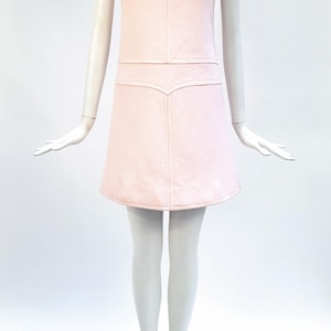 Puede incluir: Vestido rosa claro sin mangas con cuello redondo y falda acampanada. El vestido presenta detalles de costura verticales y horizontales en el corpi&ntilde;o y una costura decorativa en la cintura. El vestido se exhibe en un maniqu&iacute;.