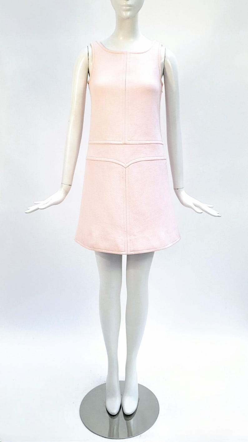 Puede incluir: Vestido rosa claro sin mangas con cuello redondo y falda acampanada. El vestido presenta detalles de costura verticales y horizontales en el corpi&ntilde;o y una costura decorativa en la cintura. El vestido se exhibe en un maniqu&iacute;.