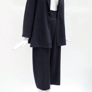 May include: A dark navy blue two-piece set consisting of a long-sleeved blazer with a notched lapel and two front buttons, paired with matching wide-leg cropped trousers. The ensemble is displayed on a white mannequin against a plain background.