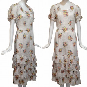 Puede incluir: Un vestido blanco con estampado floral y falda de volantes en capas. El vestido tiene un escote cuadrado y mangas abullonadas cortas.