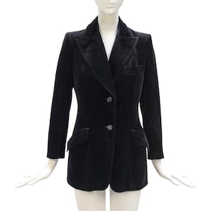 Op de afbeelding: Een zwarte fluwelen blazer met een revers, twee voorzakken en een sluiting met twee knopen. De jas met lange mouwen wordt op een mannequin gepresenteerd tegen een witte achtergrond. De blazer heeft een getailleerde pasvorm.