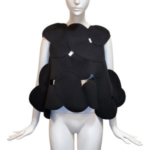 May include: A black sleeveless top with a unique design featuring overlapping circles cutouts. The top has a rounded, asymmetrical hemline.