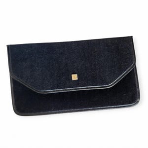 Pode incluir: Uma clutch de veludo preto com um logotipo de metal dourado. A clutch tem um fecho de aba e uma textura lisa e macia.
