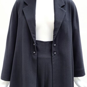 May include: A black blazer featuring a notched lapel collar, long sleeves, and a front closure with two pairs of small black buttons. The jacket has a straight hemline and a structured fit, displayed on a white mannequin against a plain white background.