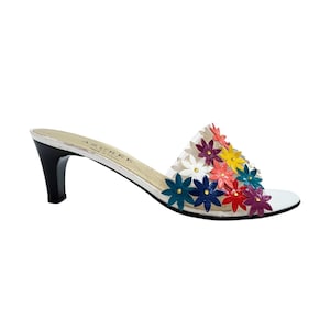 May include: A slip-on sandal with a black mid-height heel and a clear strap adorned with multi-colored floral appliqués in red, yellow, blue, purple, and white. The insole features the text AZUREE and Made in France printed in black.