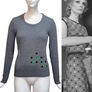 Può includere: Maglia grigia a maniche lunghe con un design geometrico nero e verde sul davanti. Il design presenta la parola "Dior" in verde.