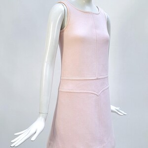 Puede incluir: Un vestido rosa claro sin mangas con cuello redondo y corpi&ntilde;o entallado. El vestido presenta un sutil patr&oacute;n texturizado y una falda acampanada. El vestido se exhibe en un maniqu&iacute;. El vestido es de estilo vintage.