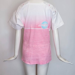 May include: A white and pink ombre t-shirt with a blue and white seagull graphic on the back. The shirt has a round neckline and short sleeves.