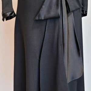 Puede incluir: Un vestido negro con un lazo de sat&eacute;n en la cintura. El vestido tiene un corpi&ntilde;o ajustado y una falda acampanada.