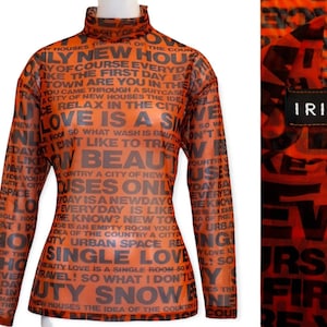 Peut inclure: Un chemisier à manches longues en maille orange avec du texte noir imprimé sur toute la surface. Le texte comprend des mots comme "new", "house", "love", "beauty", "single", et "travel". Le chemisier a un col montant et une silhouette ajustée. Le nom de la marque "IRIE" est imprimé sur une étiquette noire attachée au chemisier.