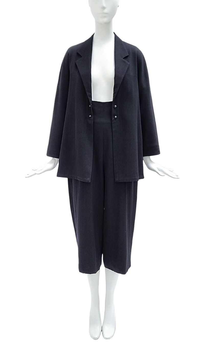 May include: A dark navy blue two-piece set consisting of a long-sleeved blazer with a notched lapel and two small silver-toned buttons at the waist, paired with matching high-waisted cropped trousers that fall below the knee in a straight cut.