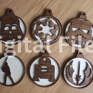 May include: Six wooden Christmas baubles featuring Star Wars characters and symbols. The baubles are round and have a white background with brown cutouts. The characters and symbols include Darth Vader, the Imperial symbol, a Stormtrooper, Luke Skywalker, R2-D2, and the Rebel Alliance symbol.